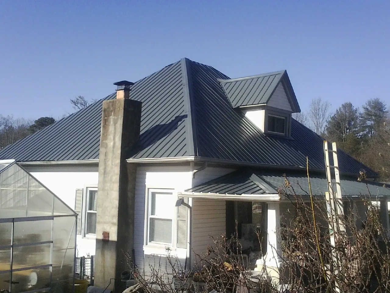 Dark blue standing seam metal roof on a white farmhouse with dormer — Slate & Tile Roof Repair by Roofing Brothers in Flat Top