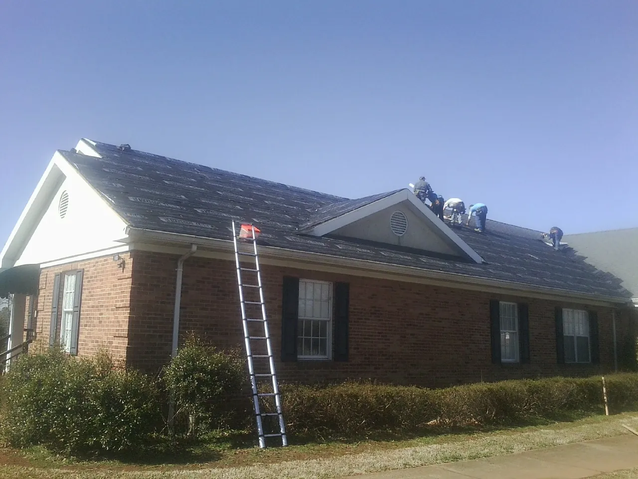 Crew tearing shingles off a brick ranch roof with a ladder set — Emergency Roof Repair work by our crew in Flat Top