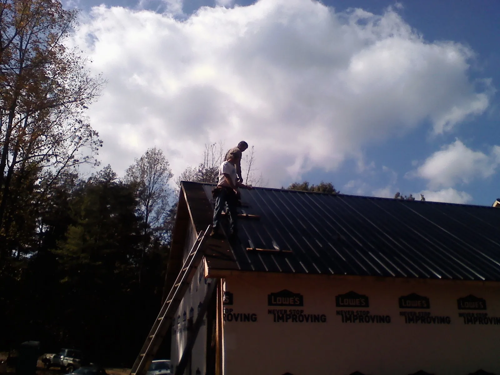 Roofer fastening dark metal panels high against a cloudy sky, from a Roof Inspection job in Flat Top