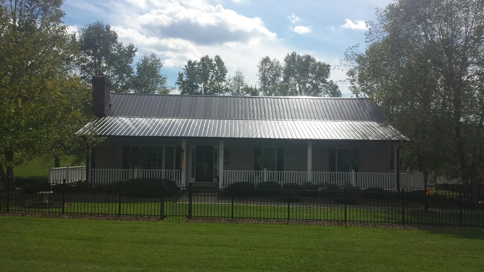 Gray metal roof on a brick ranch with a full width front porch — Gutter Guard Installation work by our crew in Flat Top