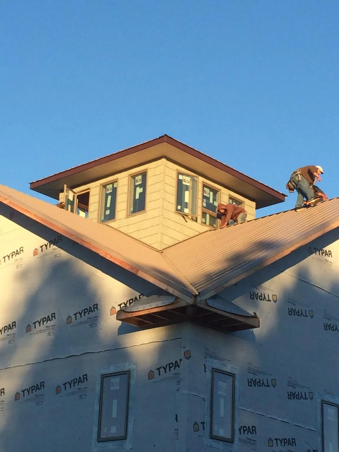 Roofers working around a rooftop cupola on a new metal roof at sunset — Roof Waterproofing in Flat Top by Roofing Brothers